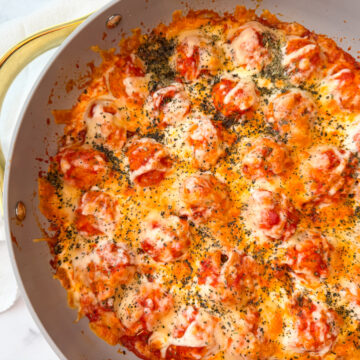 large skillet filled with meatballs, marinara, and melted mozzarella cheese and topped with basil.