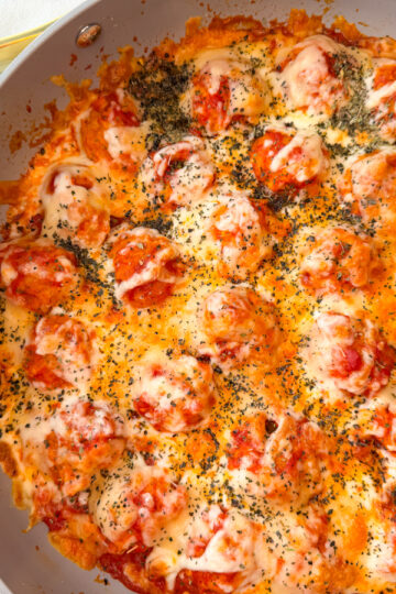 large skillet filled with meatballs, marinara, and melted mozzarella cheese and topped with basil.