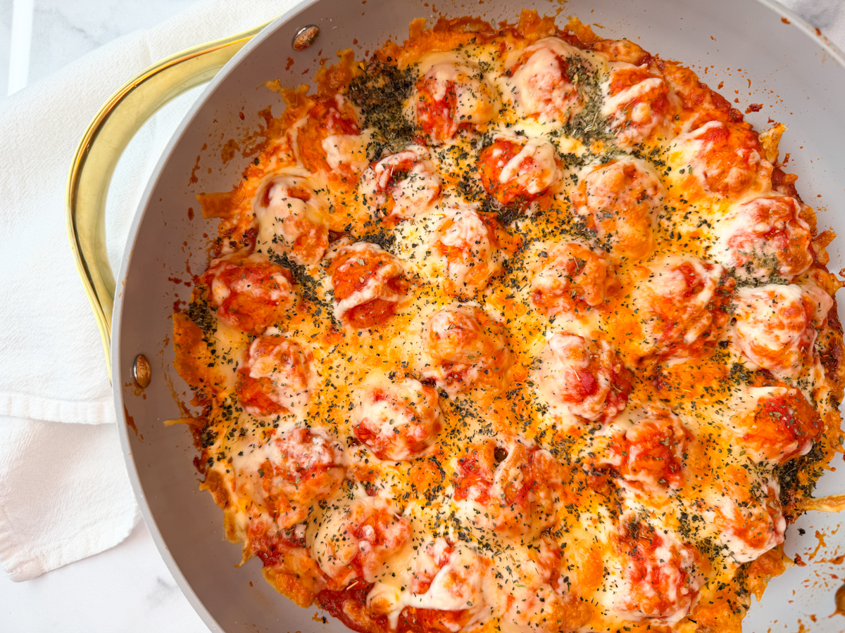 chicken meatballs in a large skillet with marinara and melted cheese. Topped with dried basil.