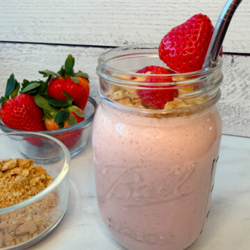 a blended strawberry cheesecake smoothie in a mason jar topped with fresh strawberries and crushed graham crackers.