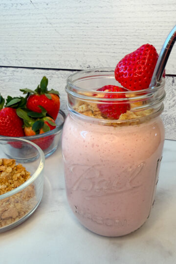 a blended strawberry cheesecake smoothie in a mason jar topped with fresh strawberries and crushed graham crackers.