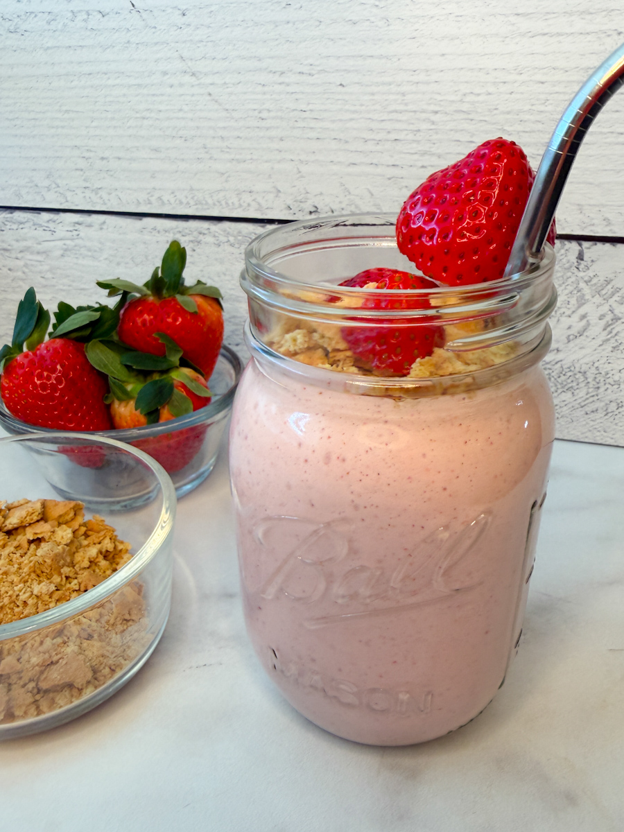 a blended strawberry cheesecake smoothie in a mason jar topped with fresh strawberries and crushed graham crackers.