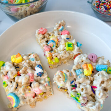 Lucky Charm Rice Krispie treats - 3 bars on a white plate with colorful marshmallows on top.