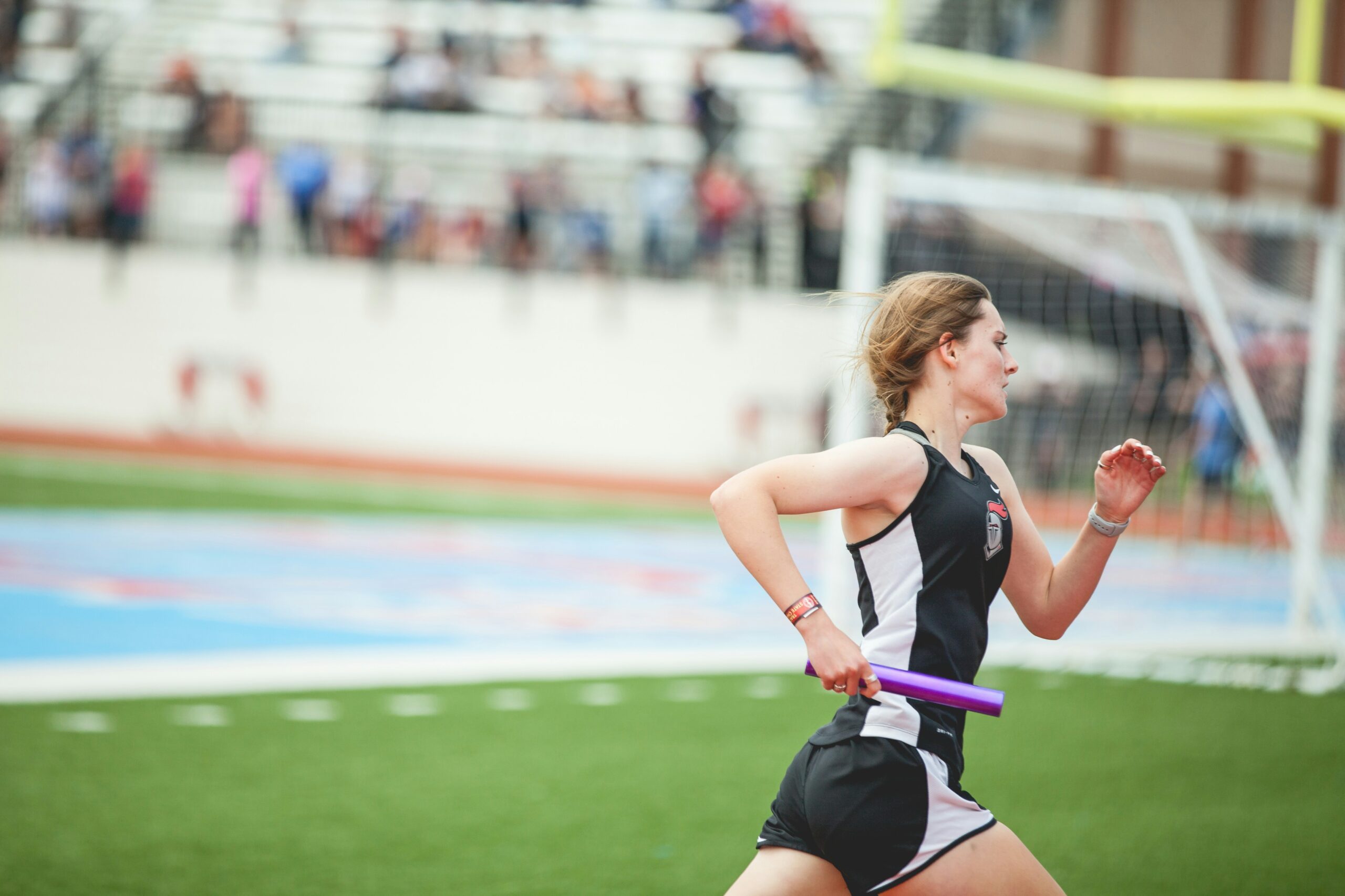 teen girl track runner racing while holding a baton