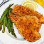 Air Fryer Lemon Parmesan Chicken on a plate with a side of green beans and lemon wedges.