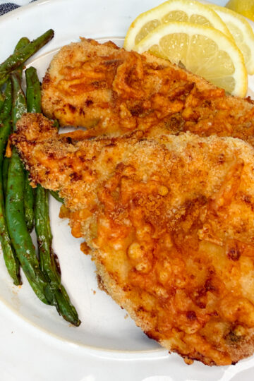 Air Fryer Lemon Parmesan Chicken on a plate with a side of green beans and lemon wedges.
