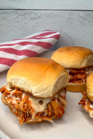 3 Chicken Parmesan Sliders on a plate with melted cheese and marinara sauce on toasted slider buns.