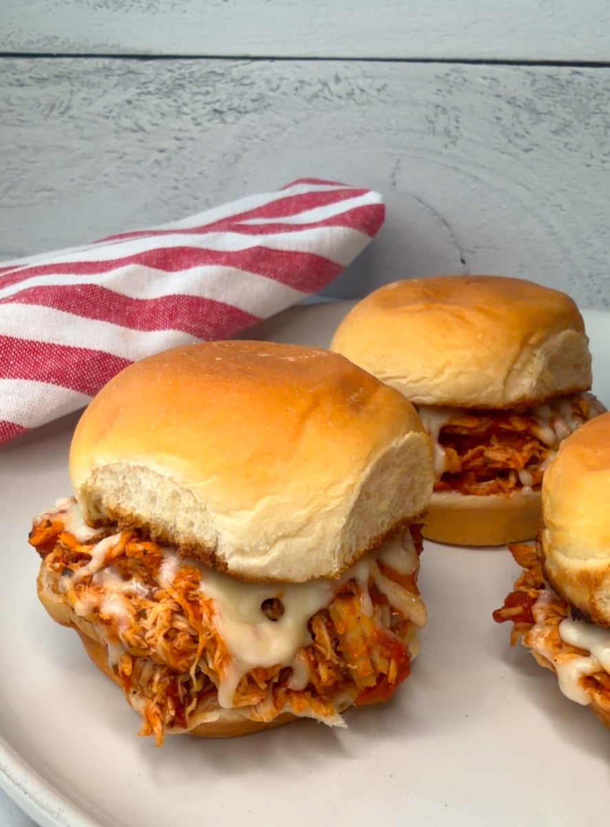 3 Chicken Parmesan Sliders on a plate with melted cheese and marinara sauce on toasted slider buns.
