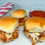 3 chicken parmesan sliders on a plate with melted cheese and toasted slider buns.