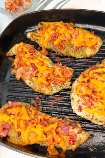 4 grilled bacon ranch chicken breasts in a grill skillet topped with crumbled bacon and melted cheddar cheese.