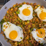 Spicy Pork Brussels Bowl in a large skillet with cooked pork, shredded brussels, and topped with 4 over easy eggs.