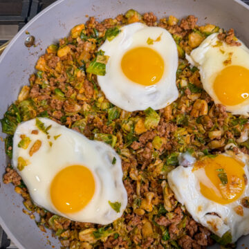 Spicy Pork Brussels Bowl in a large skillet with cooked pork, shredded brussels, and topped with 4 over easy eggs.