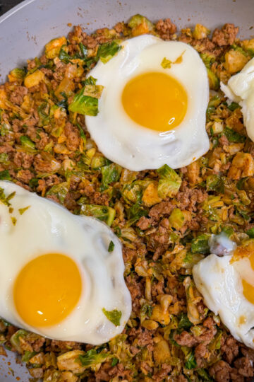 Spicy Pork Brussels Bowl in a large skillet with cooked pork, shredded brussels, and topped with 4 over easy eggs.