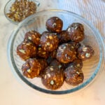 Mint chocolate protein balls rolled into a glass bowl. There are about 15 balls in the bowl with Andes mint chips.