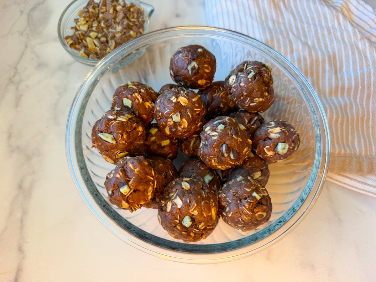 Mint chocolate protein balls rolled into a glass bowl. There are about 15 balls in the bowl with Andes mint chips.